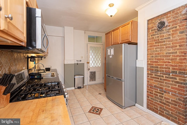 kitchen featuring backsplash, brick wall, light tile patterned floors, stainless steel appliances, and a sink