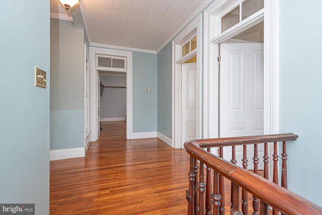 corridor with wood finished floors, baseboards, and ornamental molding