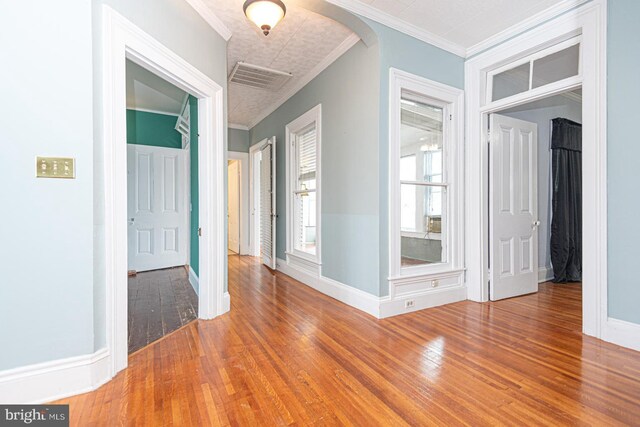 interior space with visible vents, crown molding, baseboards, hardwood / wood-style floors, and arched walkways