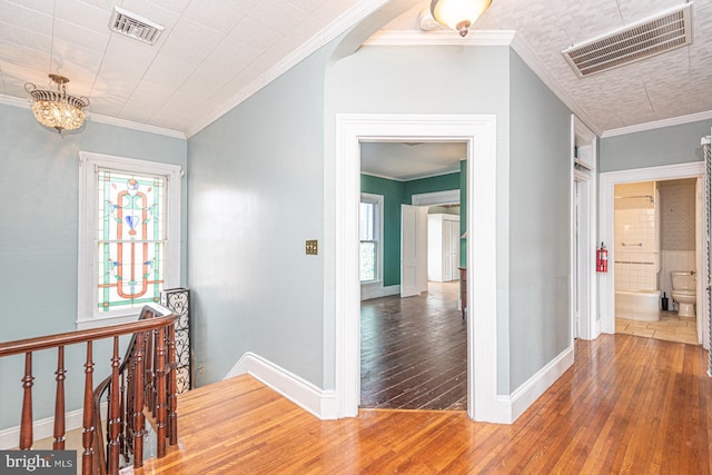 hall with hardwood / wood-style floors, crown molding, an upstairs landing, and visible vents