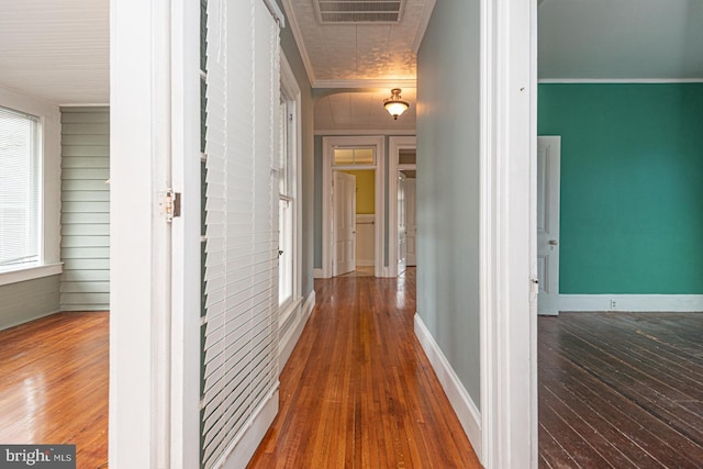 corridor featuring visible vents, baseboards, hardwood / wood-style floors, and crown molding