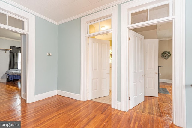 hallway with light wood-type flooring, crown molding, and baseboards