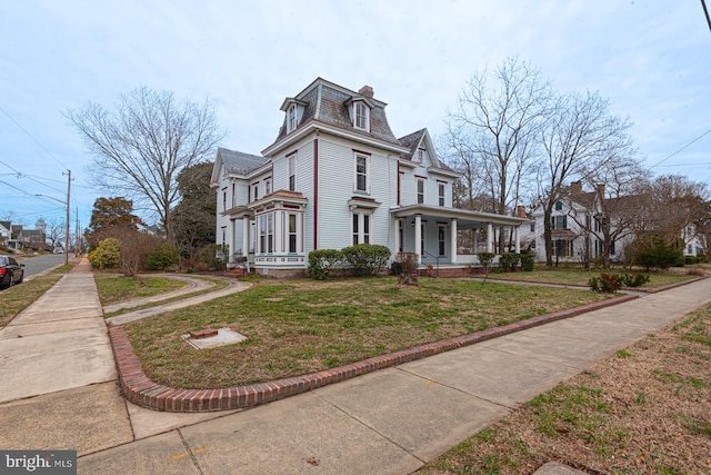 view of side of home featuring a porch, a lawn, mansard roof, and a chimney