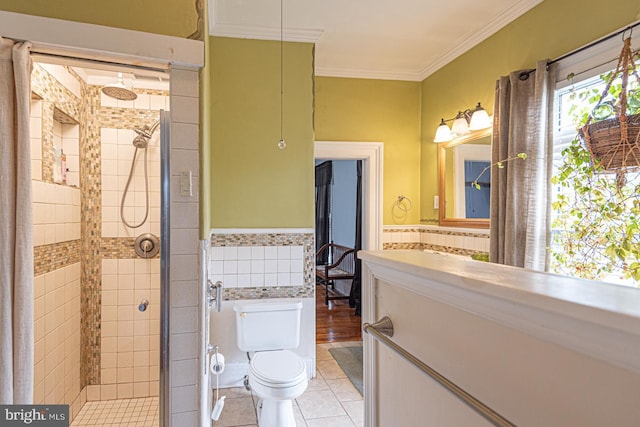 bathroom featuring a shower stall, crown molding, a wainscoted wall, toilet, and tile walls