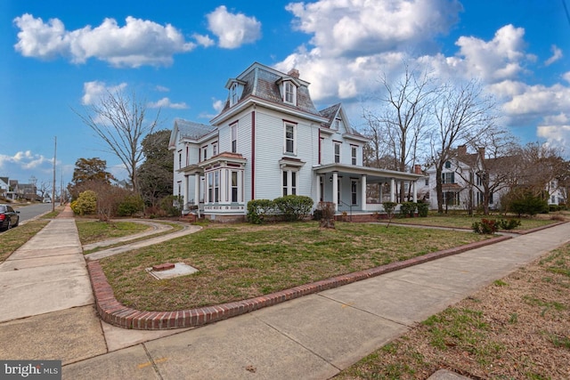 view of side of home with mansard roof, a high end roof, a lawn, and a porch