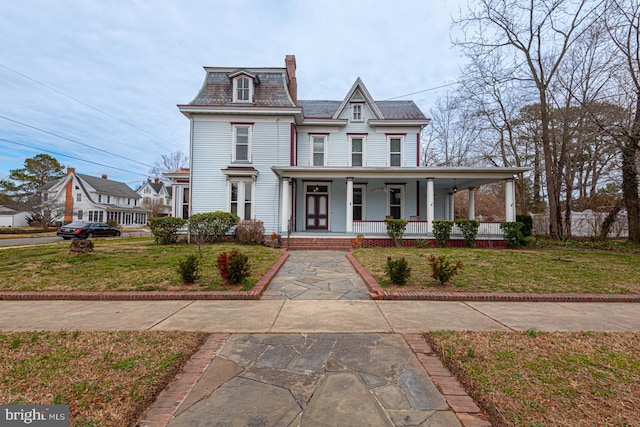 view of front of property with mansard roof, a chimney, covered porch, and a front yard