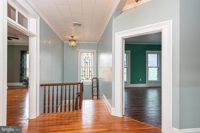 hall featuring hardwood / wood-style floors, an upstairs landing, visible vents, and ornamental molding