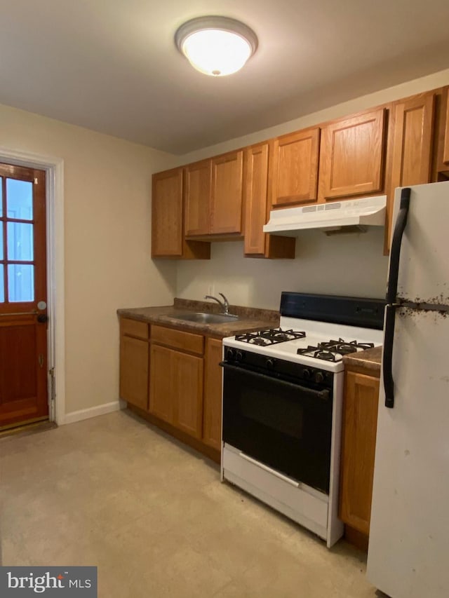 kitchen featuring dark countertops, freestanding refrigerator, a sink, under cabinet range hood, and gas range