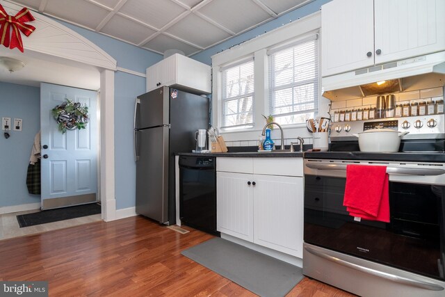 kitchen featuring under cabinet range hood, stainless steel appliances, wood finished floors, white cabinetry, and a sink