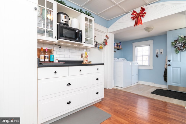 kitchen featuring washing machine and clothes dryer, light wood finished floors, tasteful backsplash, dark countertops, and white cabinets