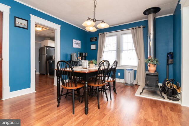 dining space featuring baseboards, wood finished floors, a wood stove, and ornamental molding