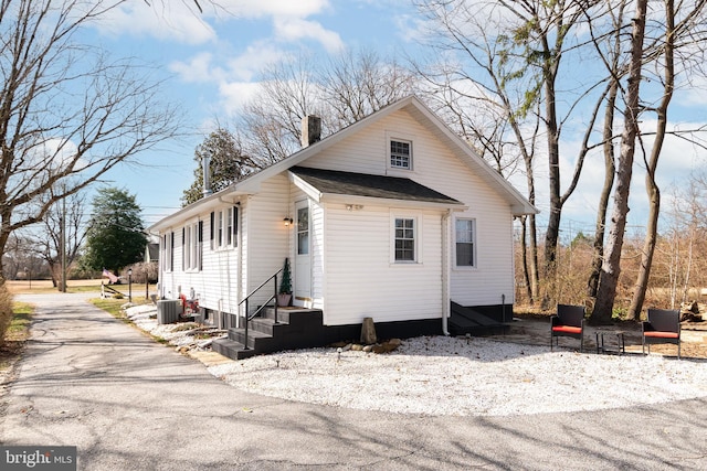 view of home's exterior with roof with shingles, central AC, a chimney, and entry steps