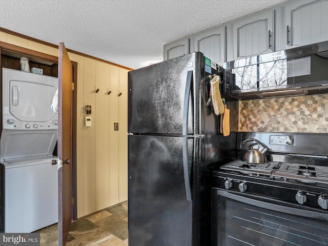 kitchen with wood walls, a textured ceiling, black appliances, and stacked washer and dryer