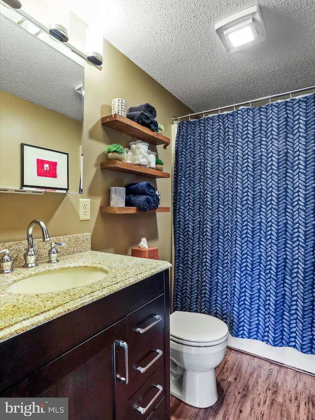 bathroom with a shower with curtain, toilet, a textured ceiling, wood finished floors, and vanity