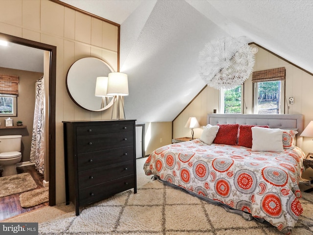 bedroom with lofted ceiling, a textured ceiling, and ensuite bath