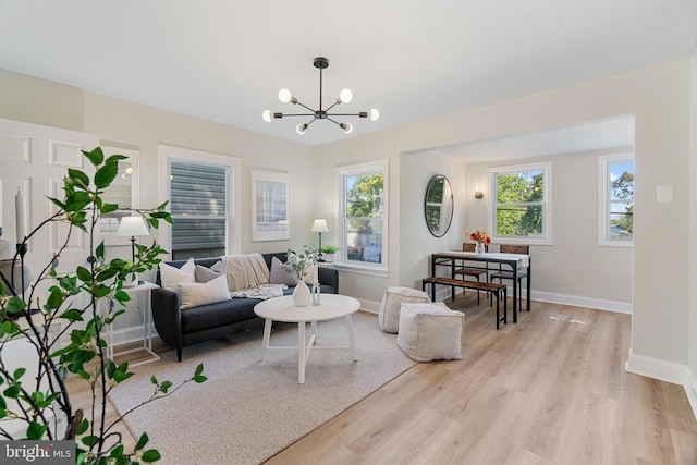 living room featuring light wood-style floors, plenty of natural light, a notable chandelier, and baseboards