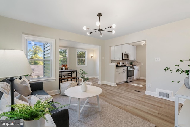 living room featuring light wood finished floors, visible vents, a chandelier, and baseboards