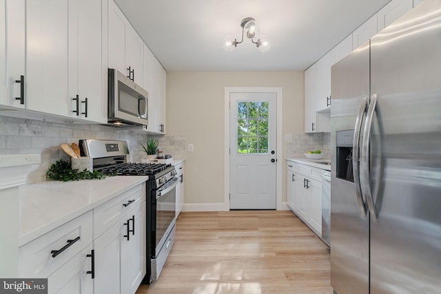 kitchen with light wood-style flooring, backsplash, appliances with stainless steel finishes, white cabinets, and baseboards