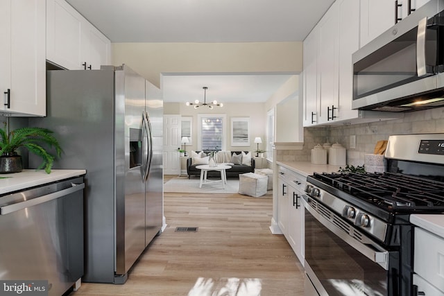 kitchen featuring a notable chandelier, tasteful backsplash, stainless steel appliances, white cabinets, and light countertops