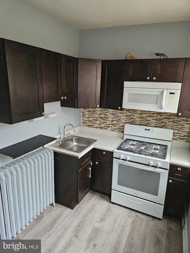 kitchen featuring white appliances, radiator, a sink, light countertops, and light wood-type flooring