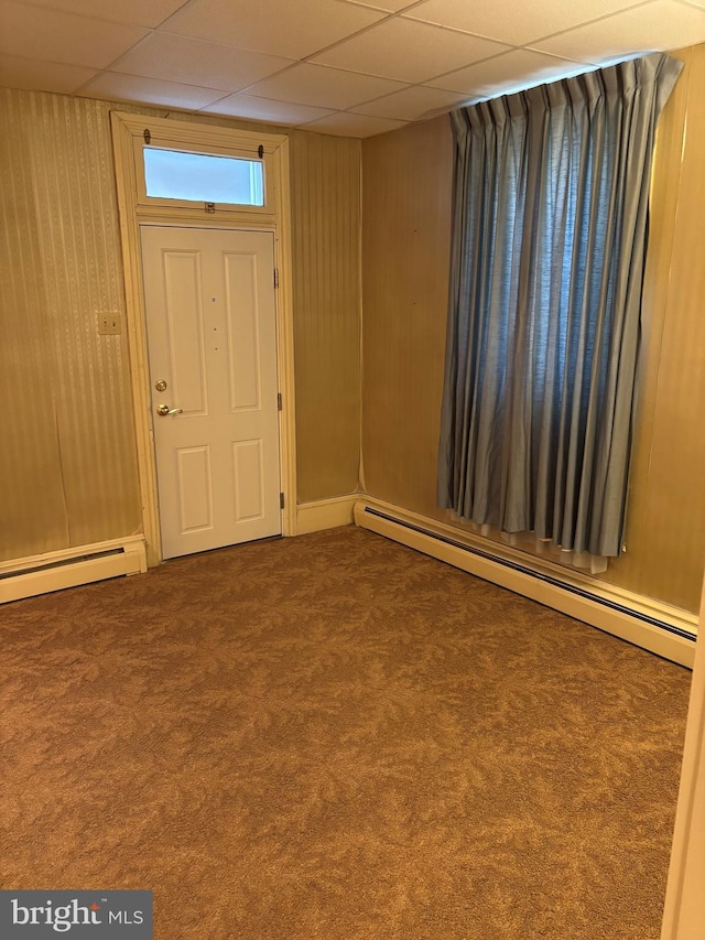 carpeted entryway with wooden walls, a drop ceiling, and a baseboard radiator