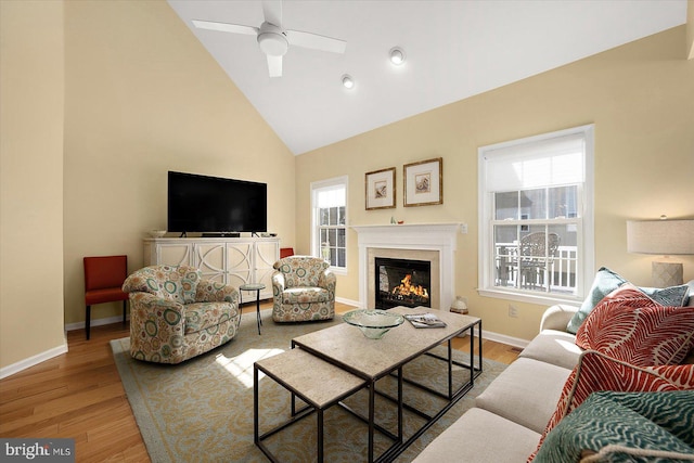 living room with a warm lit fireplace, baseboards, and wood finished floors