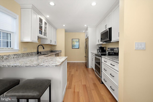 kitchen featuring light wood finished floors, a sink, stainless steel appliances, white cabinets, and glass insert cabinets