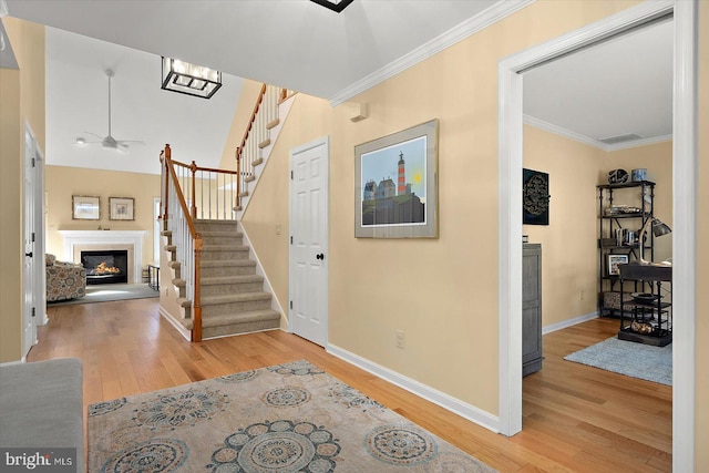 stairway featuring a glass covered fireplace, wood finished floors, baseboards, and ornamental molding