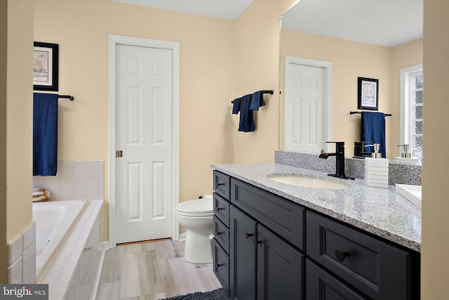 full bath featuring vanity, a relaxing tiled tub, toilet, and wood finished floors