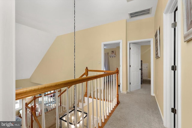 hall with an upstairs landing, visible vents, baseboards, and carpet