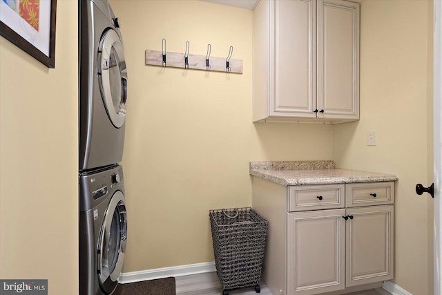 laundry room featuring cabinet space, stacked washing maching and dryer, and baseboards