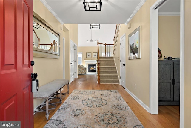 entrance foyer featuring ornamental molding, stairway, a lit fireplace, light wood finished floors, and baseboards