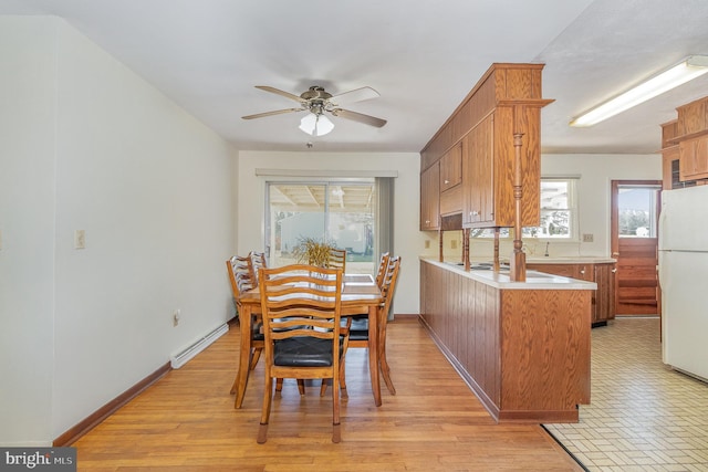 kitchen with brown cabinetry, light wood finished floors, a peninsula, freestanding refrigerator, and baseboard heating