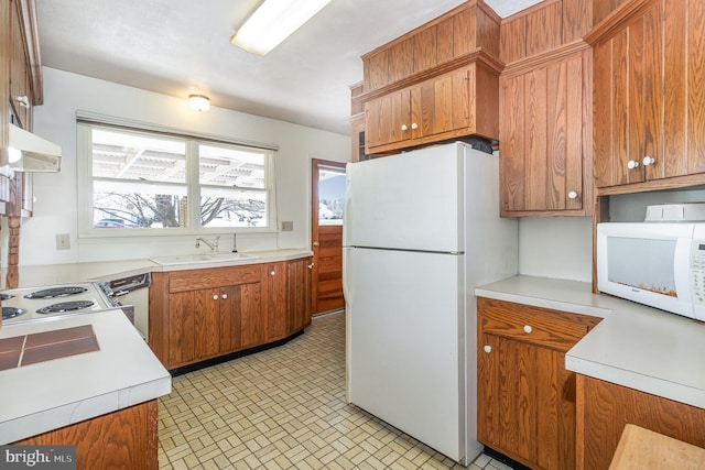 kitchen featuring under cabinet range hood, light countertops, brown cabinets, white appliances, and a sink