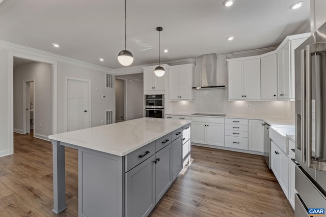 kitchen with gray cabinetry, a kitchen island, wall chimney range hood, light wood-type flooring, and stainless steel appliances