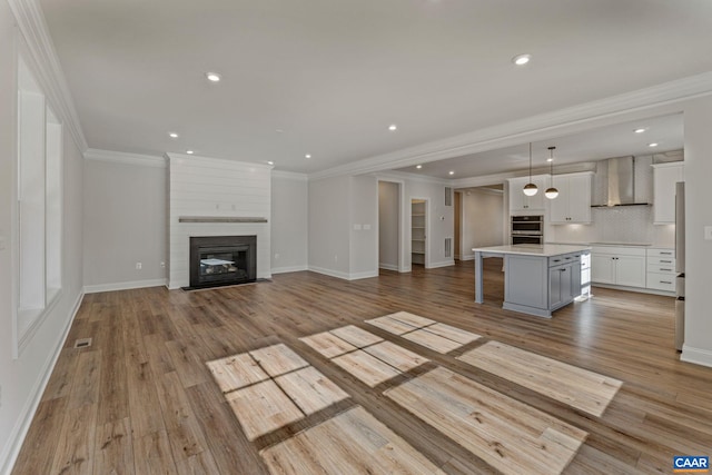 unfurnished living room with visible vents, a large fireplace, baseboards, ornamental molding, and light wood-style flooring