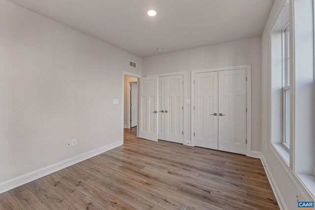 unfurnished bedroom with light wood-style floors, baseboards, two closets, and visible vents