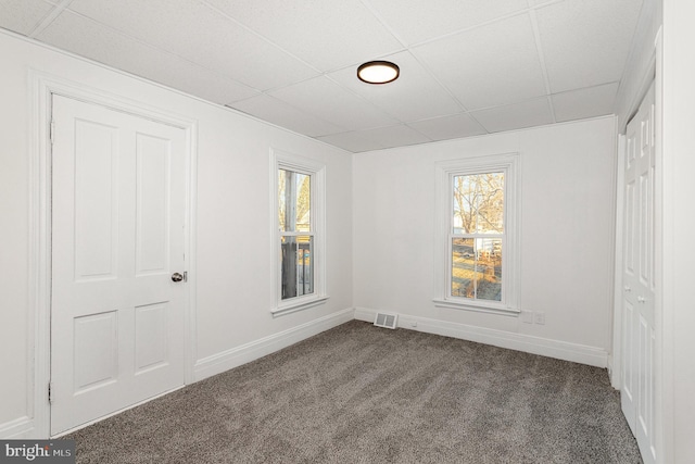 unfurnished bedroom with visible vents, a paneled ceiling, baseboards, and dark colored carpet