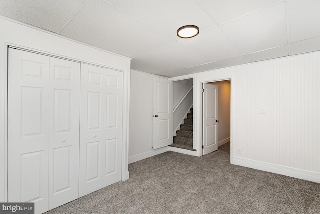 below grade area with stairway, a paneled ceiling, baseboards, and carpet flooring