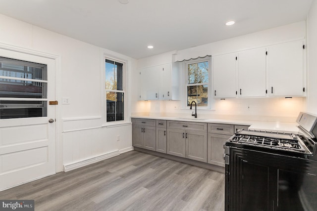 kitchen with a baseboard radiator, light wood-style flooring, gray cabinets, a sink, and gas range oven