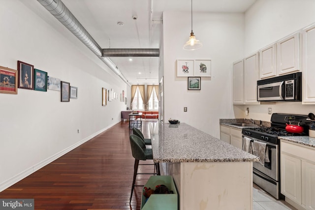 kitchen with baseboards, a breakfast bar, light stone counters, appliances with stainless steel finishes, and light wood-style floors