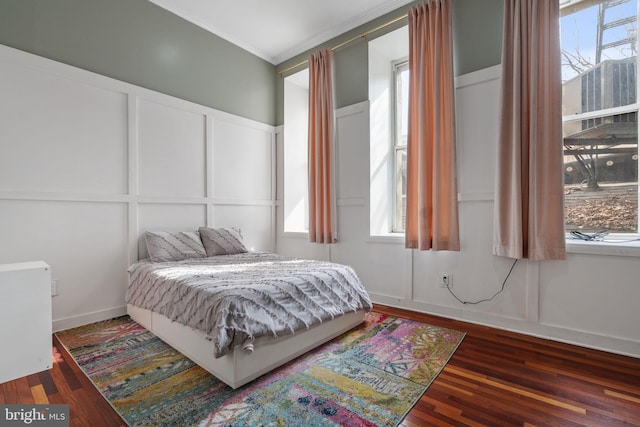 bedroom with multiple windows, wood finished floors, crown molding, and a decorative wall