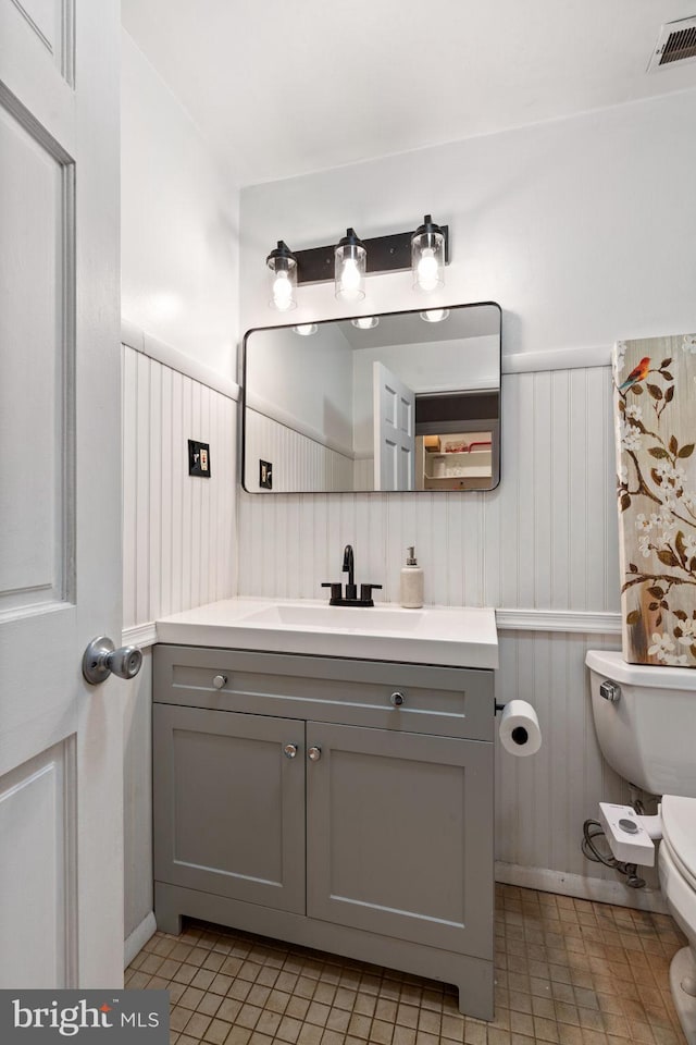 half bath with visible vents, wainscoting, toilet, and vanity