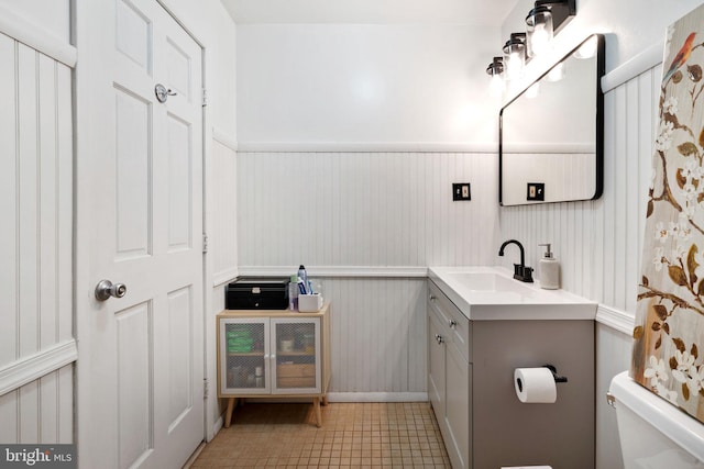 bathroom featuring tile patterned flooring, wainscoting, toilet, and vanity