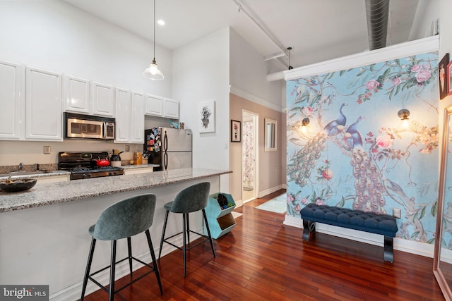 kitchen with a breakfast bar, light stone counters, white cabinets, stainless steel appliances, and dark wood-style flooring