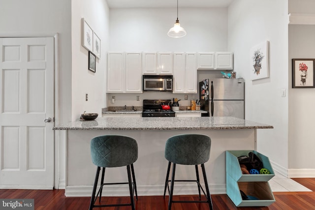 kitchen with light stone counters, a breakfast bar, dark wood-style flooring, stainless steel appliances, and white cabinets