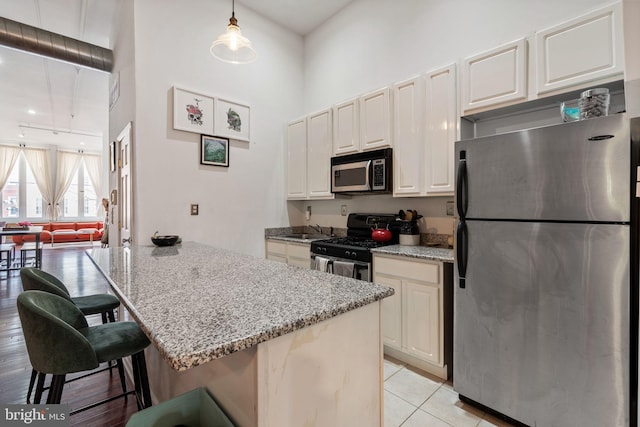 kitchen with light stone counters, a breakfast bar, stainless steel appliances, hanging light fixtures, and a towering ceiling