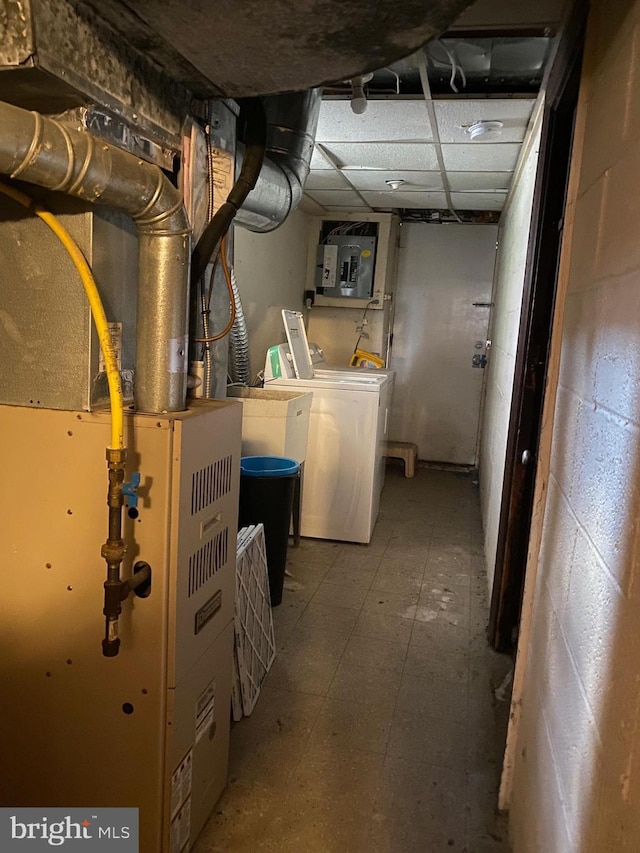 unfinished below grade area featuring heating unit, electric panel, a paneled ceiling, tile patterned floors, and washing machine and dryer