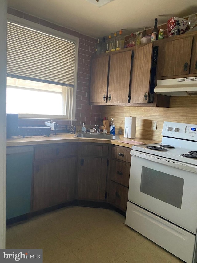 kitchen with under cabinet range hood, a sink, white range with electric stovetop, light countertops, and decorative backsplash