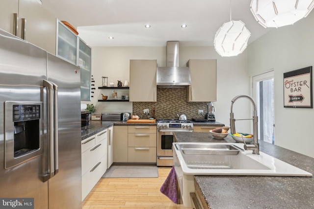 kitchen featuring a sink, tasteful backsplash, stainless steel appliances, light wood-style floors, and wall chimney range hood